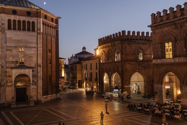 Cremona, Itália. Vista da Piazza del Comune, o coração medieval da cidade e uma das praças mais belas da Itália. A praça abriga um conjunto monumental único, que inclui a Catedral românica, famosa por seus afrescos, a torre sineira Torrazzo, o Batistério, o Palazzo del Comune e a Loggia dei Militi. Conhecida como o berço da fabricação de violinos, Cremona é terra natal de luthiers lendários como Andrea Amati, Antonio Stradivari e Giuseppe Guarneri. Desde o século XVI, a tradição cremonesa de fabricação de violinos moldou os padrões acústicos e formais do violino moderno e é hoje reconhecida como Patrimônio Cultural Imaterial da Humanidade pela UNESCO.